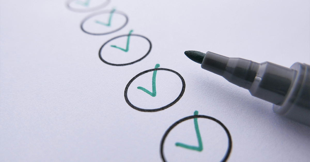 Caneta marcando itens de uma checklist em folha branca, representando revisão para carta argumentativa da UFU